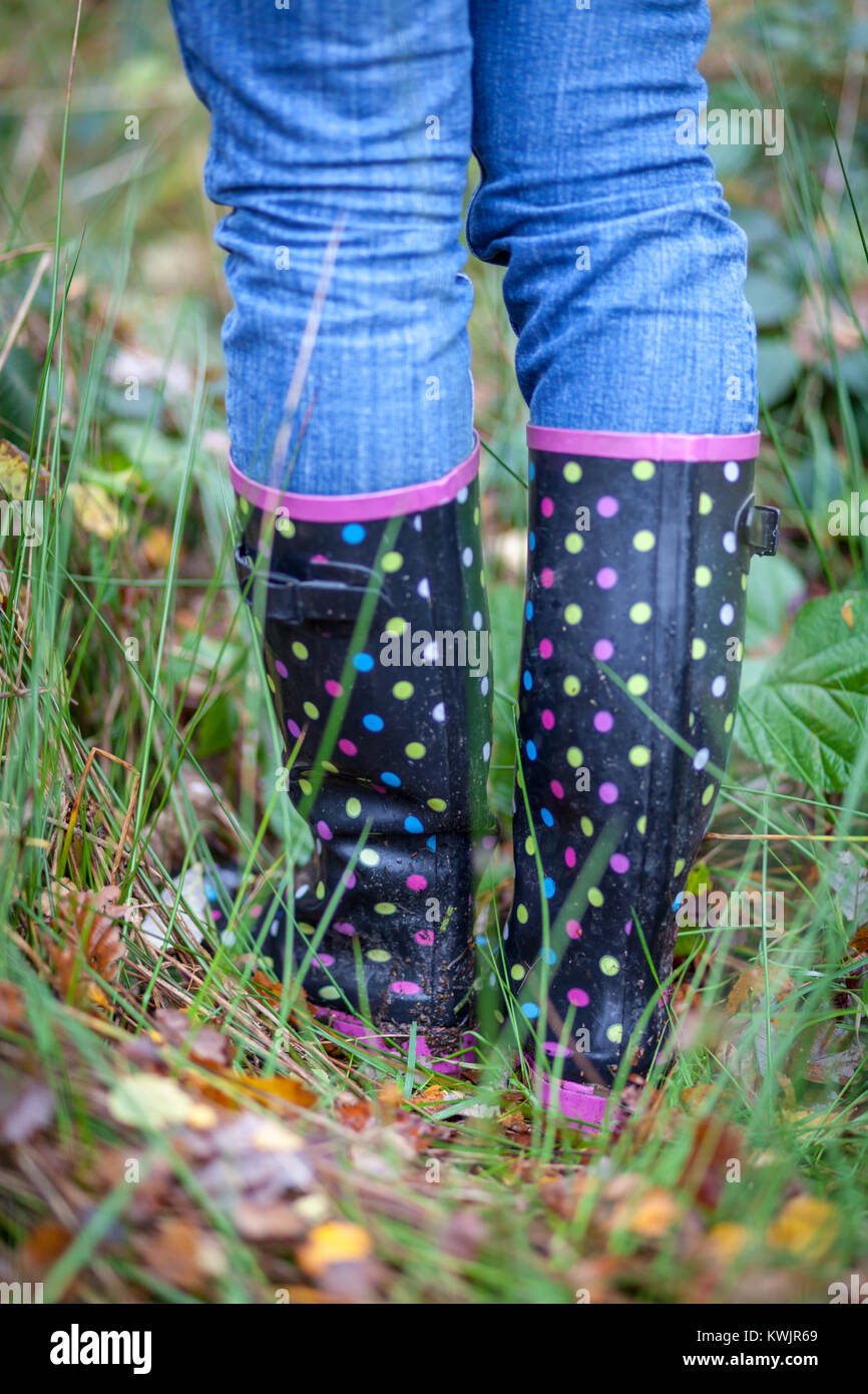 A pair of spotty wellingtons are worn by someone wearing blue jeans while walking through long wild grass Stock Photo