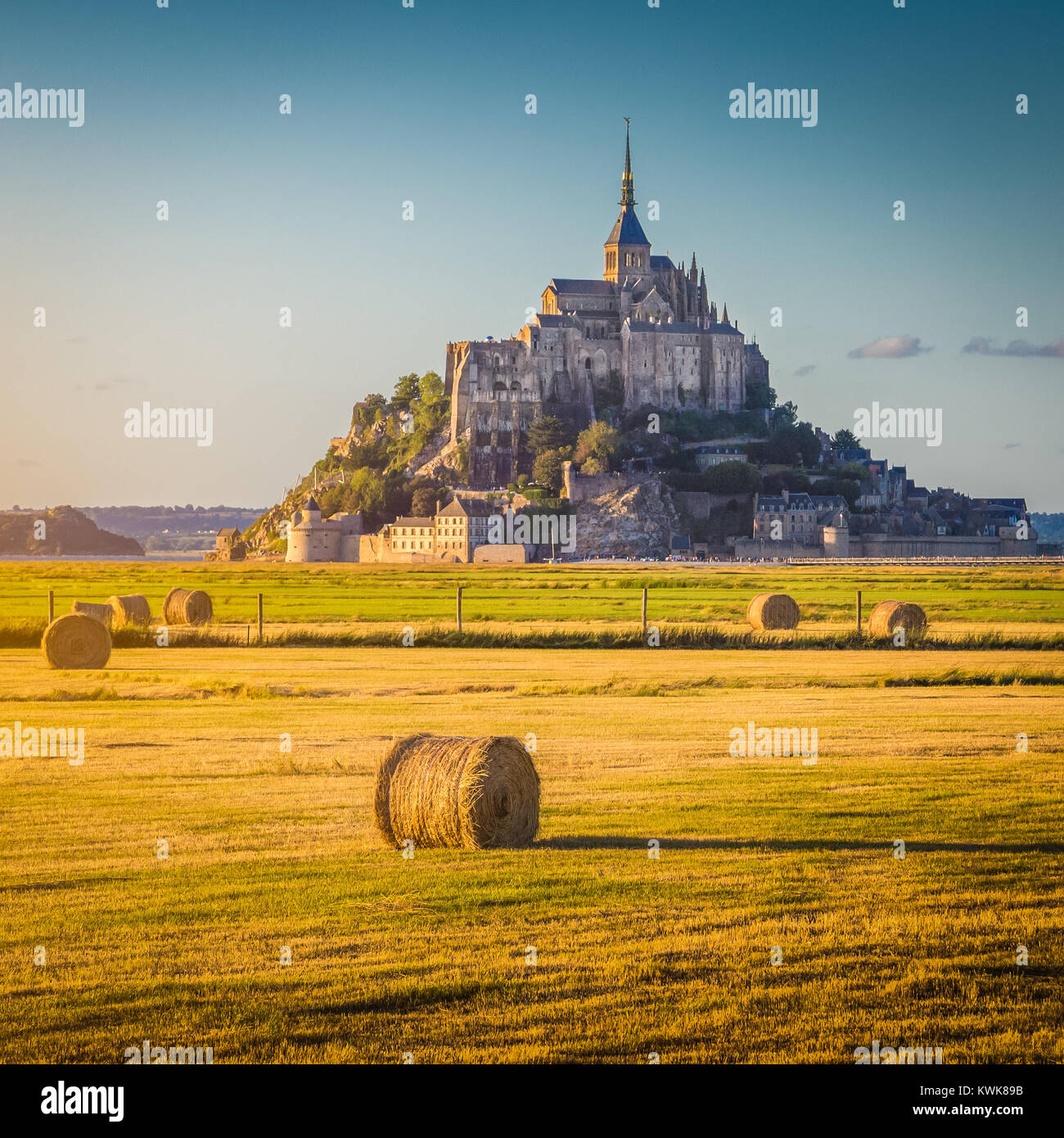 Beautiful view of famous historic Le Mont Saint-Michel in golden evening light at sunset in summer with hay bales on fields, Normandy, France Stock Photo