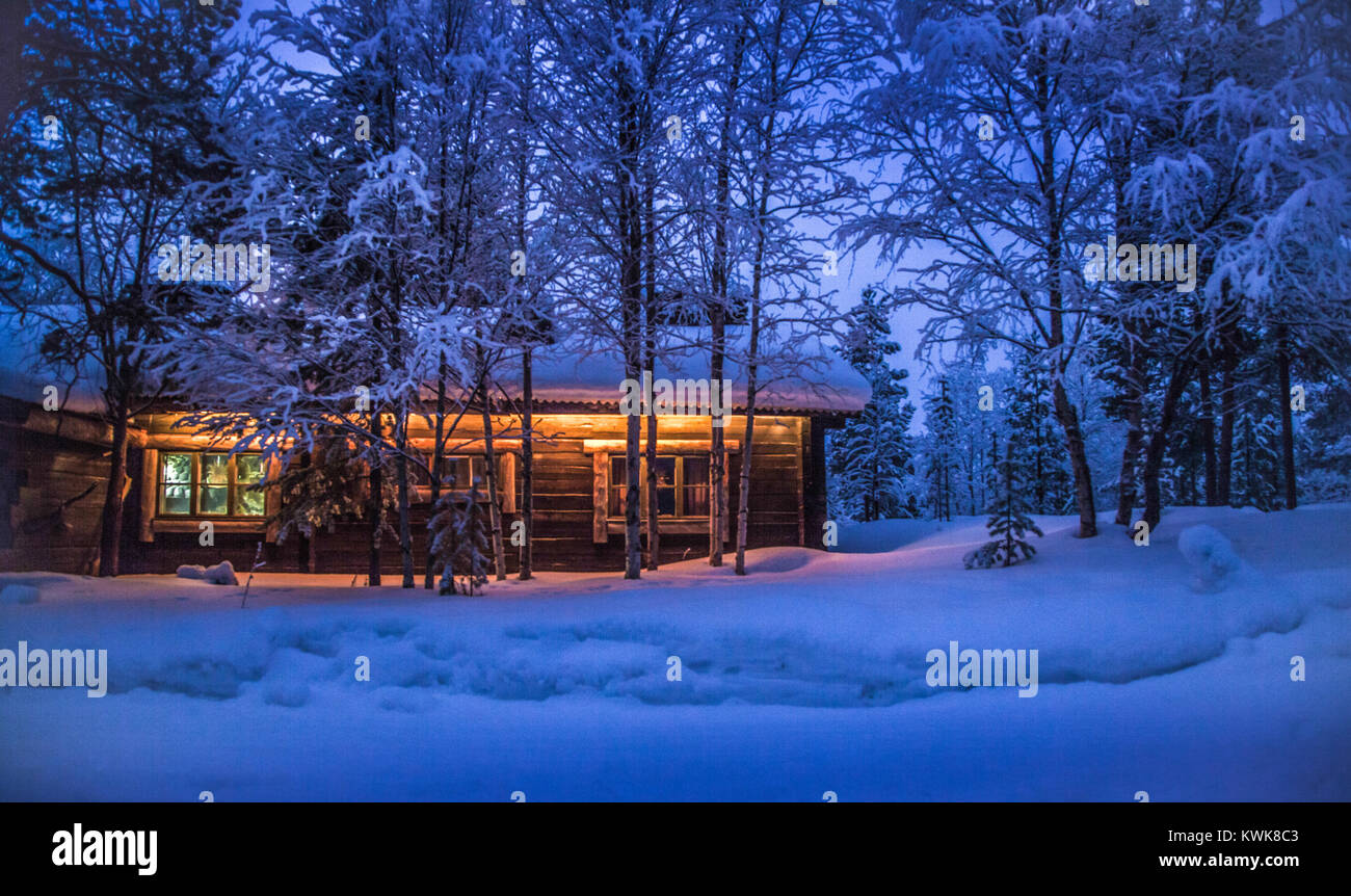 Romantic view of old traditional wooden forest cabin in the woods embedded in scenic northern winter wonderland scenery in beautiful mystic twilight Stock Photo