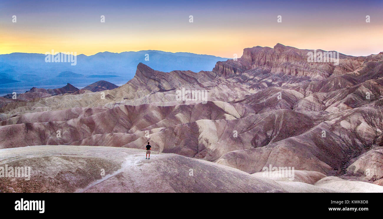Panoramic view of a hiker standing at famous Zabriskie Point viewpoint in golden evening light at sunset, Death Valley National Park, California, USA Stock Photo