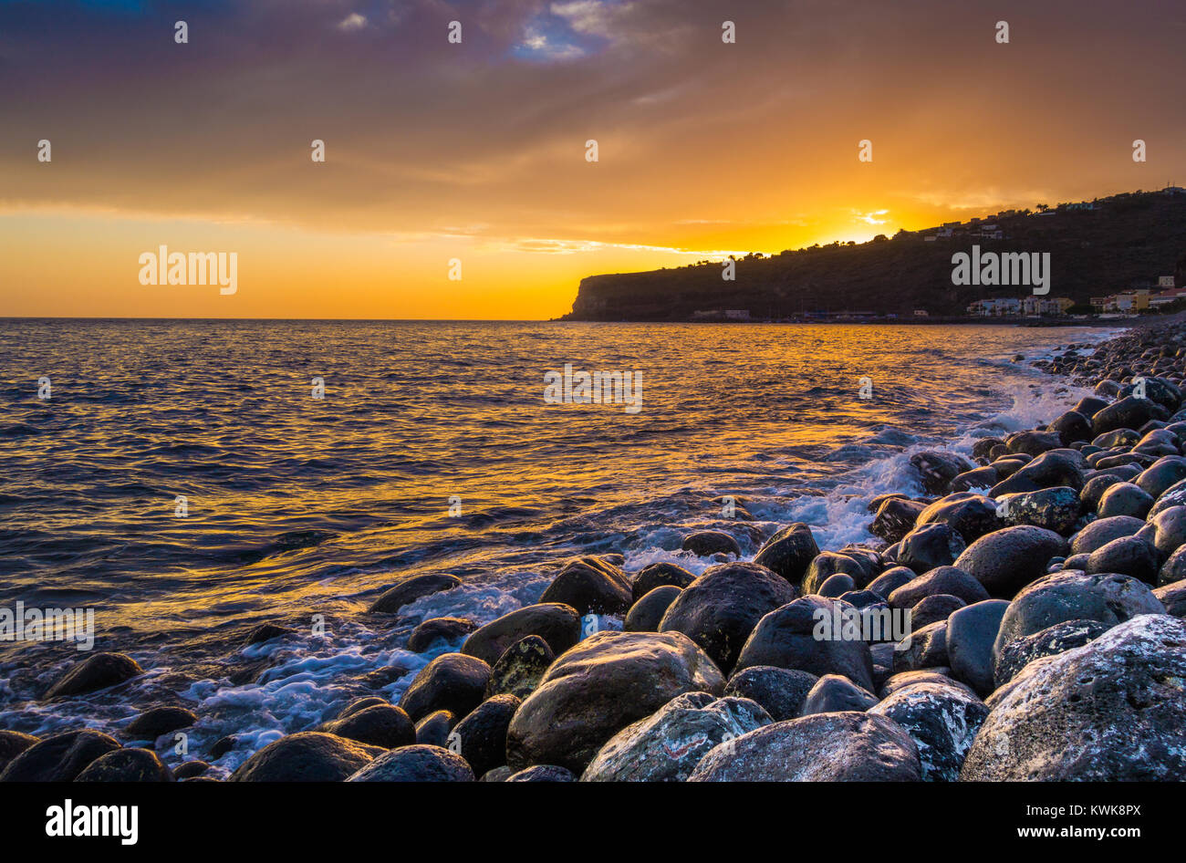 Panorama view of amazing ocean scenery with rocks on a beach in beautiful golden evening light at sunset with blue sky, clouds and sunlight lens flare Stock Photo