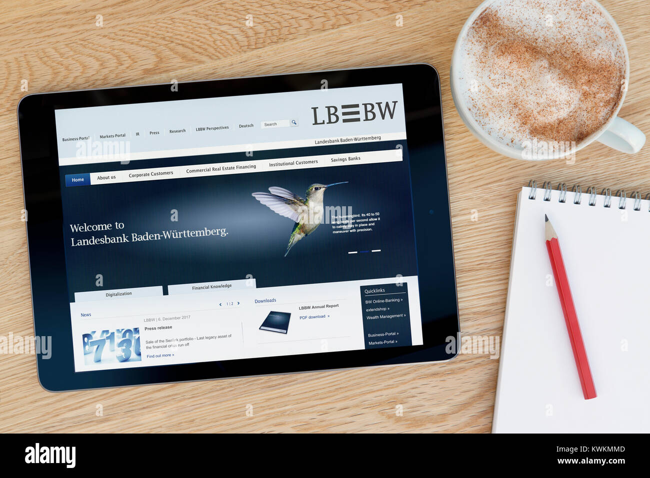 The LBBW (Landesbank Baden-Württemberg) website on an iPad tablet device, on a wooden table beside a notepad, pencil and cup of coffee -Editorial only Stock Photo