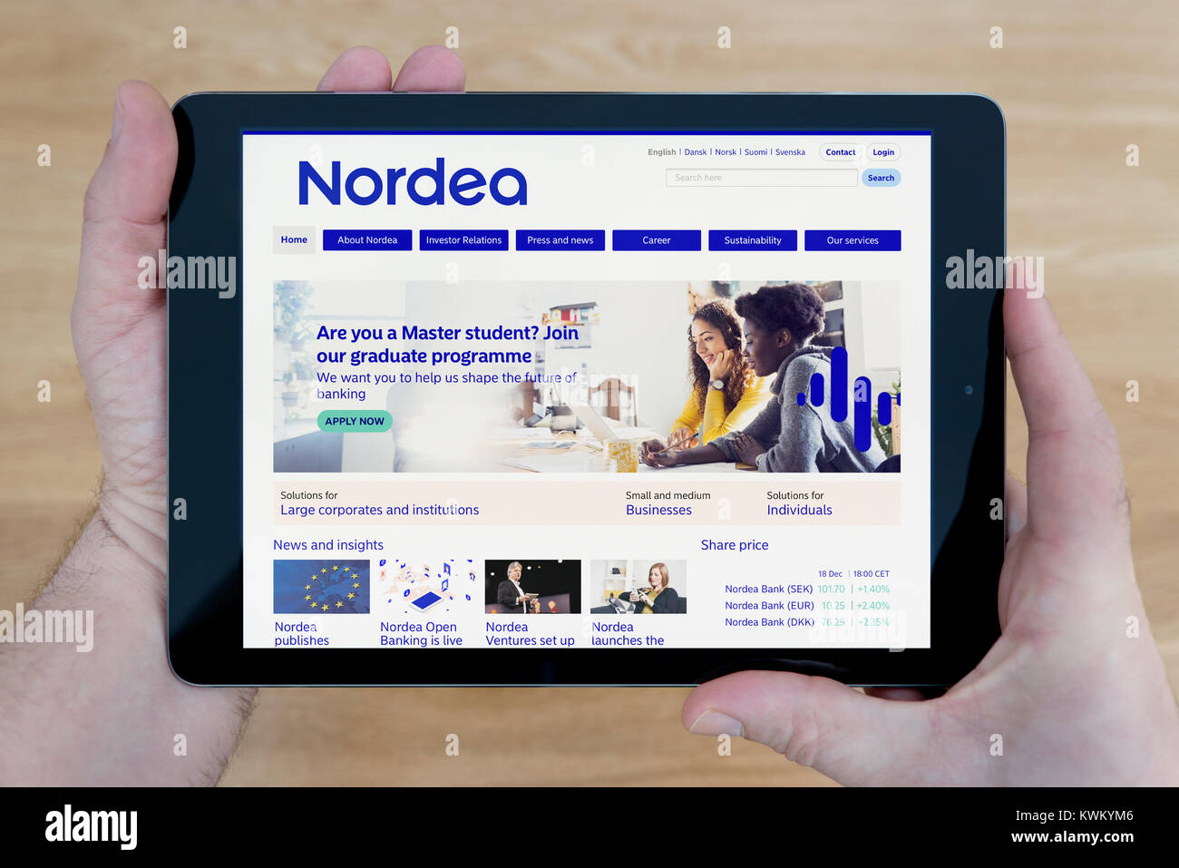 A man looks at the Nordea bank website on his iPad tablet device, over a wooden table top background (Editorial use only) Stock Photo