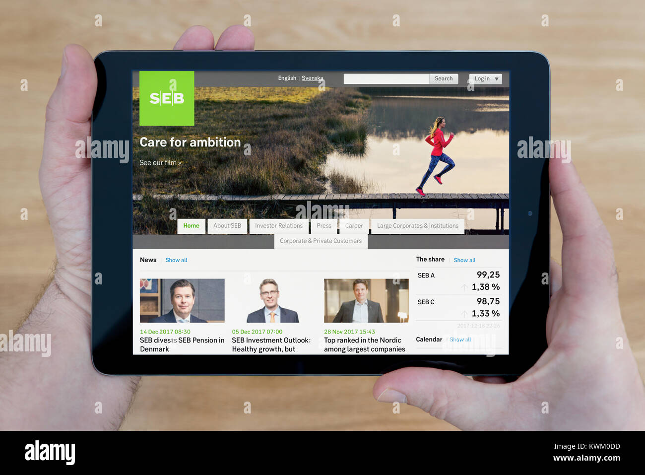 A man looks at the SEB Group (Skandinaviska Enskilda Banken) website on his iPad tablet device, over a wooden table top background (Editorial  only) Stock Photo
