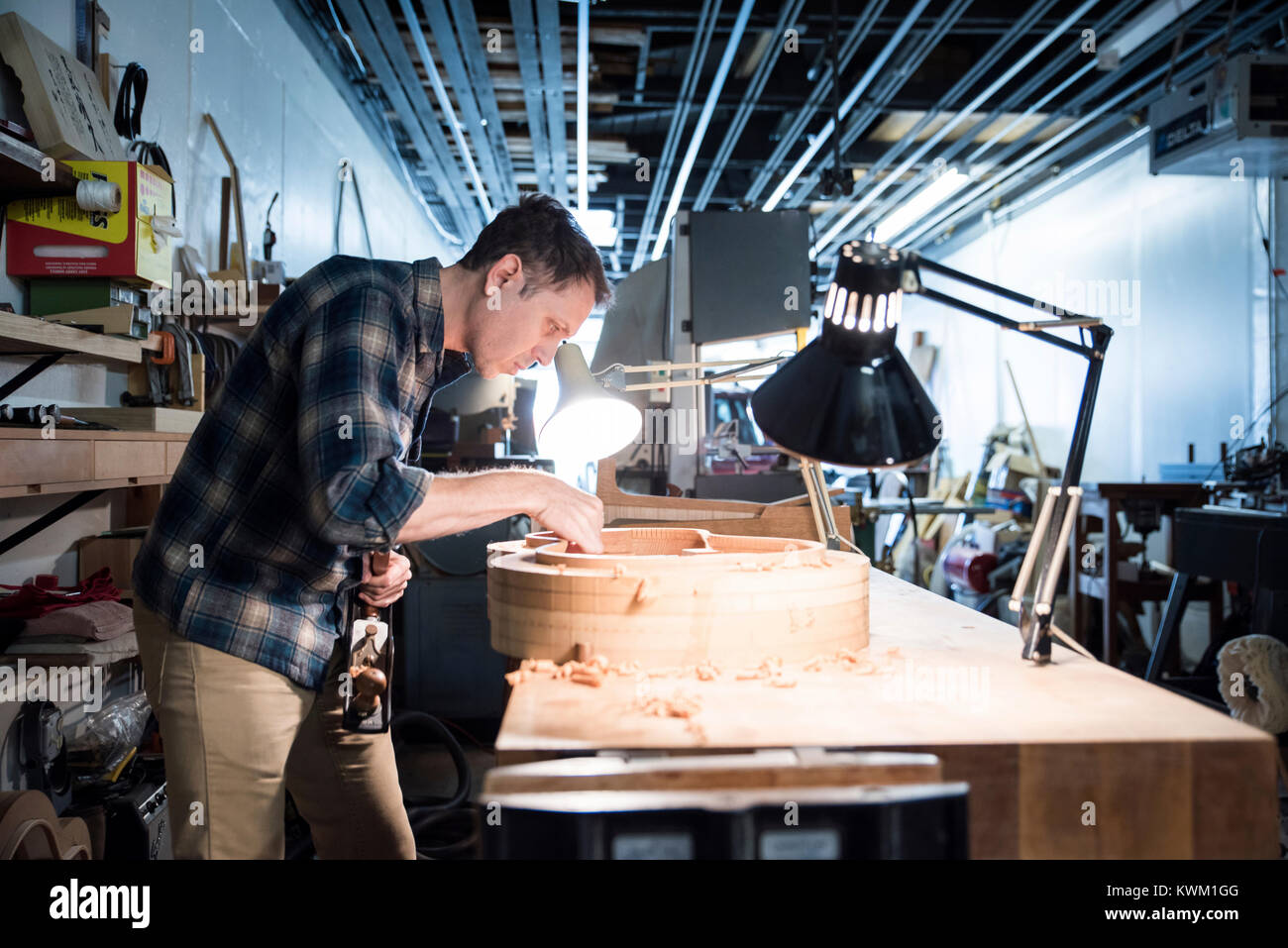Side view of worker making guitar while standing in workshop Stock Photo