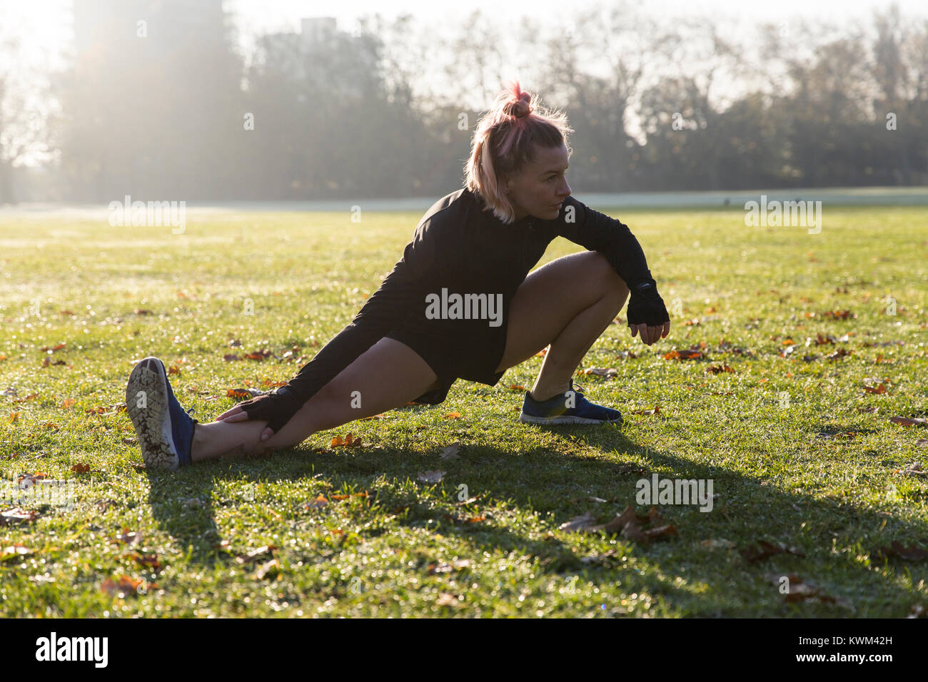 Confident woman stretching legs on grassy field at park during sunny ...