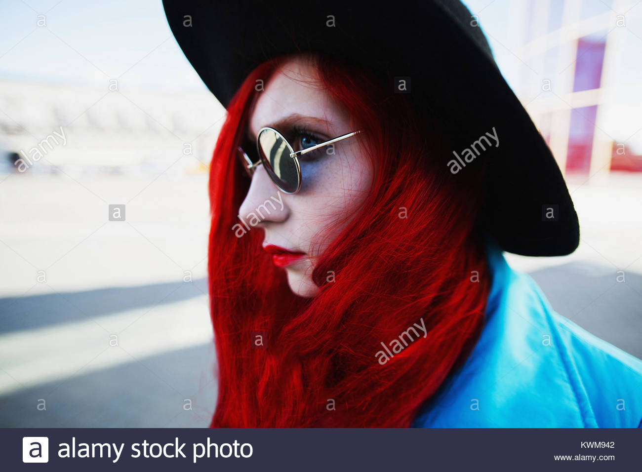 Woman With Red Curly Hair In Blue Coat And Black Round Glasses On