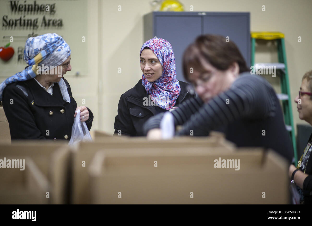 Davenport, Iowa, USA. 4th Dec, 2017. Marwa Genena of Bettendorf, center, and Chapter Leader Lisa Killinger, left, talk while packing bags of food for local students at River Bend Foodbank in Davenport on Monday, December 4, 2017. The local chapter of the Sisterhood of Salaam Shalom took part in a national event showing solidarity by bringing American Jewish and Muslim women together to perform acts of charity together as a part of National Sadaqah-Tzedakah Day. The chapter chose to focus on hunger insecurity as their focus for this year's project and worked to pack bags of food for kids Stock Photo
