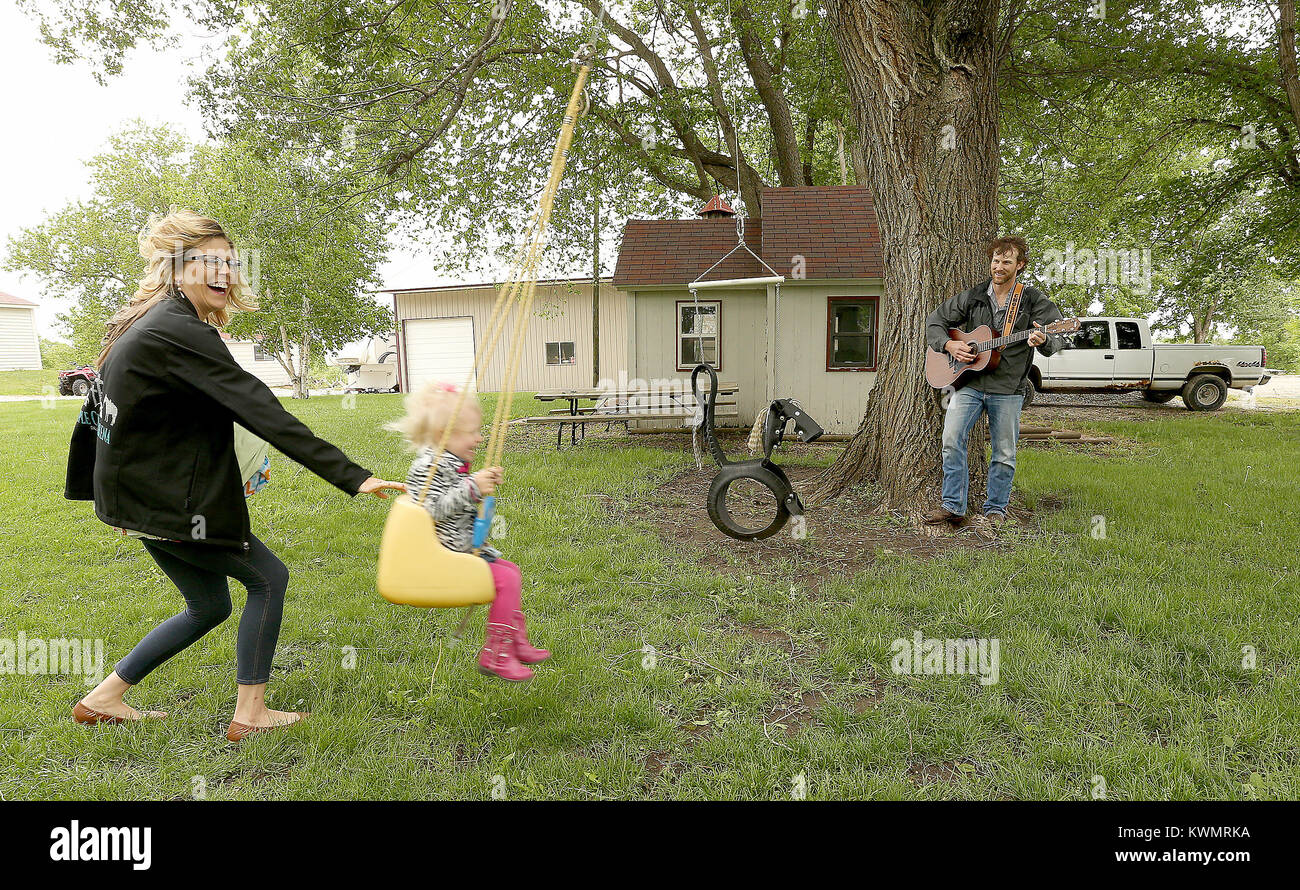 Dallas Center, Iowa, USA. 21st May, 2017. Jordanne Fry holds their son Brayton while pushing Avery 2 on the swing as Curtis plays his guitar under the tree, Sunday, May 21, 2017, on their farm in Dallas Center, Iowa. Credit: John Schultz/Quad-City Times/ZUMA Wire/Alamy Live News Stock Photo