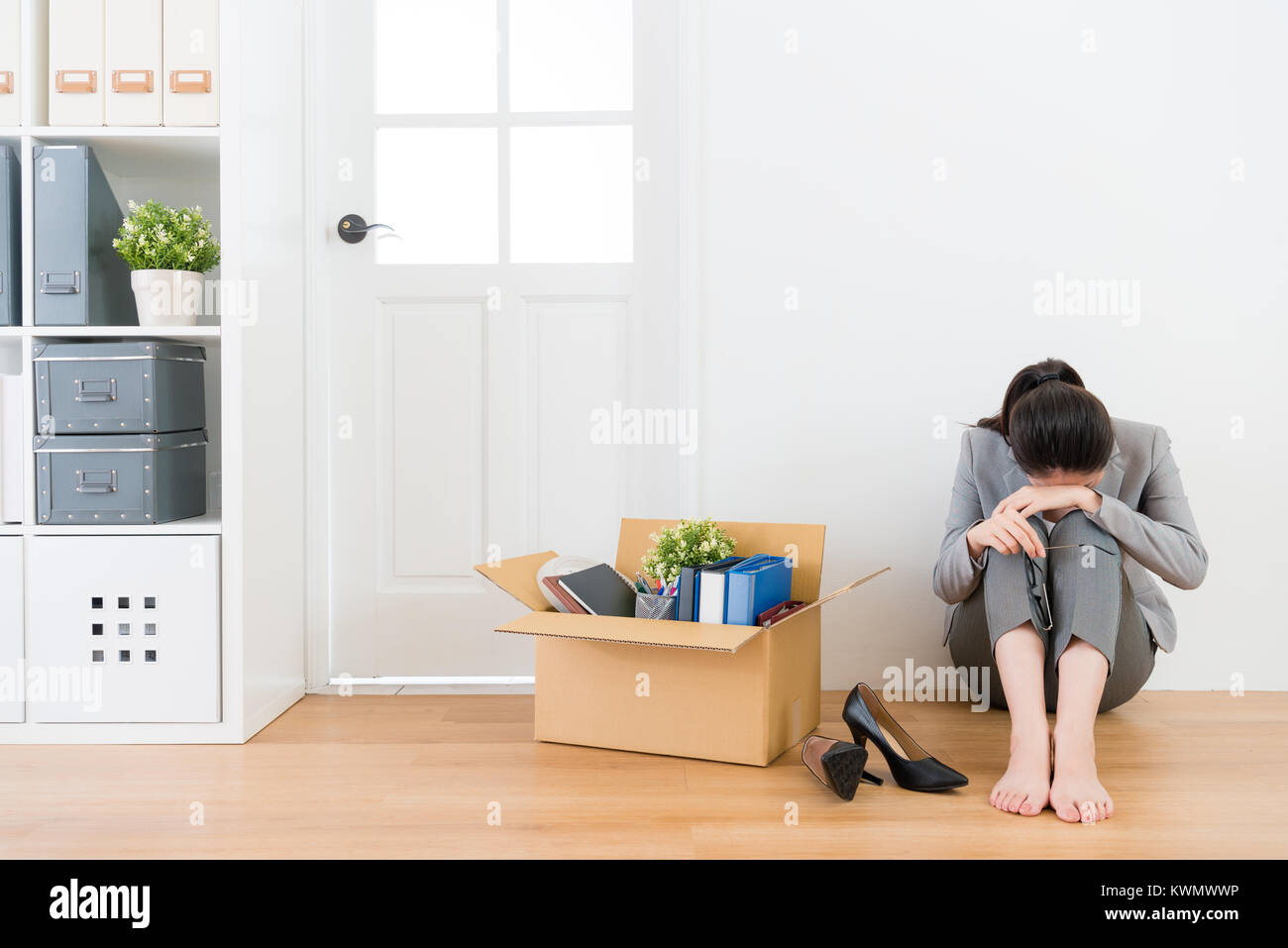 sadness pretty business manager woman unemployed sitting on wood floor crying with personal office items box. Stock Photo