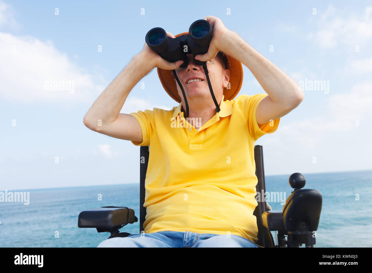 Disabled man with binocular sitting on the wheelchair. Sea on the background Stock Photo