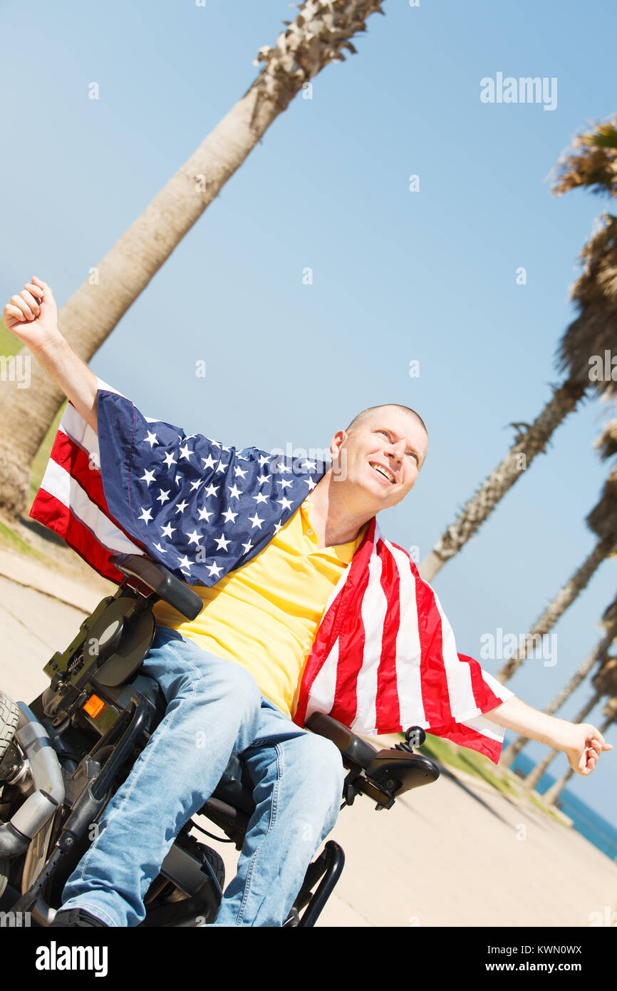 Disabled man sitting in wheelchair with flag of USA showing freedom Stock Photo