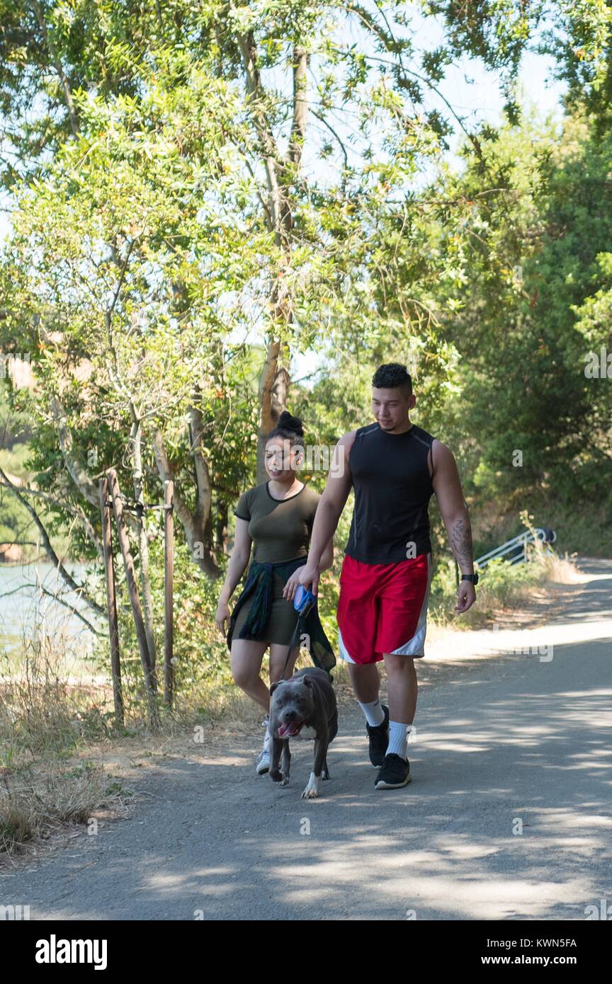 A Millennial generation couple walks with a pit bull down a trail at Lake Chabot Regional Park, an East Bay Regional Park in the San Francisco Bay Area town of San Leandro, California, July 16, 2017. Stock Photo