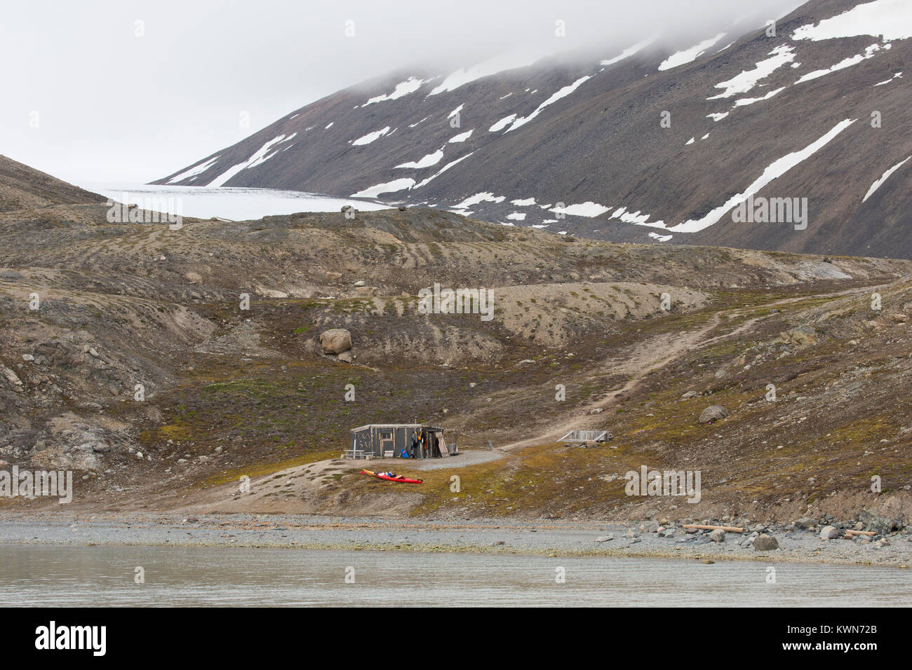 Sea kayaker using Texas Bar as shelter, old fur trapper cabin at Worsleyhamna, Liefdefjorden / Liefdefjord, Svalbard / Spitsbergen, Norway Stock Photo