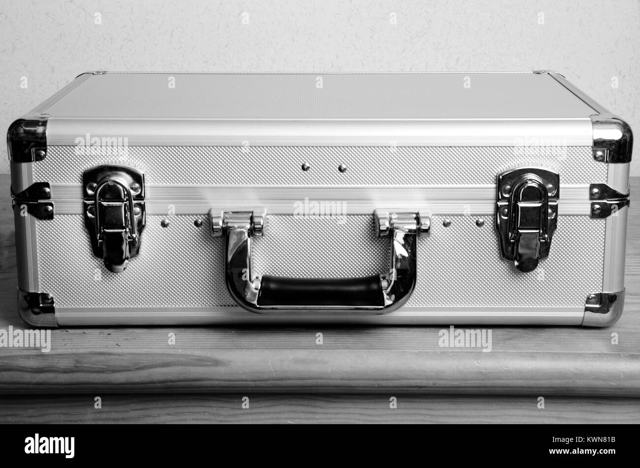 Closed metal suitcase placed on wooden furniture : front view Stock Photo