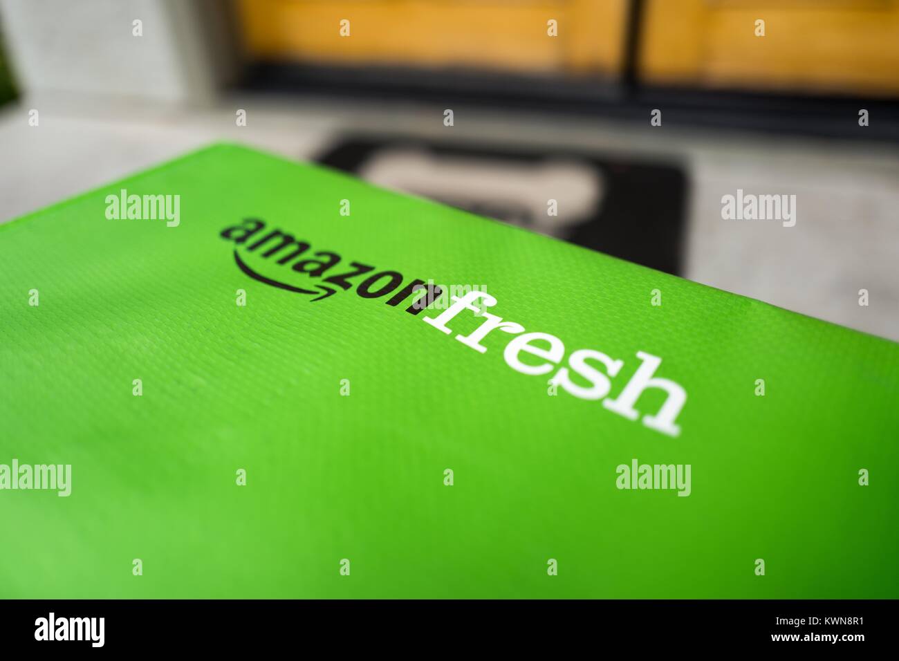 Green cold pack tote for Amazon Fresh grocery delivery service, with Amazon logo and text listing groceries which may be ordered using the service, on the doorstep of a suburban home in the San Francisco Bay Area town of San Ramon, California, April 11, 2017. In June of 2017, Amazon announced that it would acquire the upscale grocery chain Whole Foods Market to expand its offerings in the grocery industry. Stock Photo
