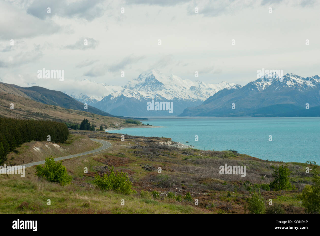 Iconic Mount Cook/Aoraki, snow capped with Mount Cook Road and vividly blue Lake Pukaki in foreground. Sunny, blue sky. Spring/ early Summer. Stock Photo