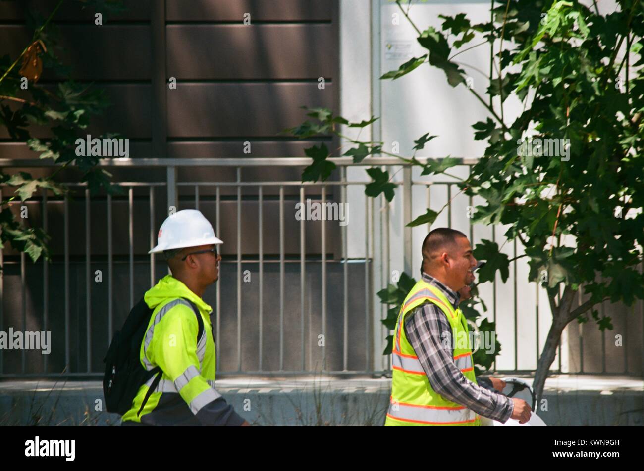 Construction workers with hard hats and high visibility vests walk near the construction zone at the Apple Park, known colloquially as 'The Spaceship', the new headquarters of Apple Inc in the Silicon Valley town of Cupertino, California, July 25, 2017. Stock Photo