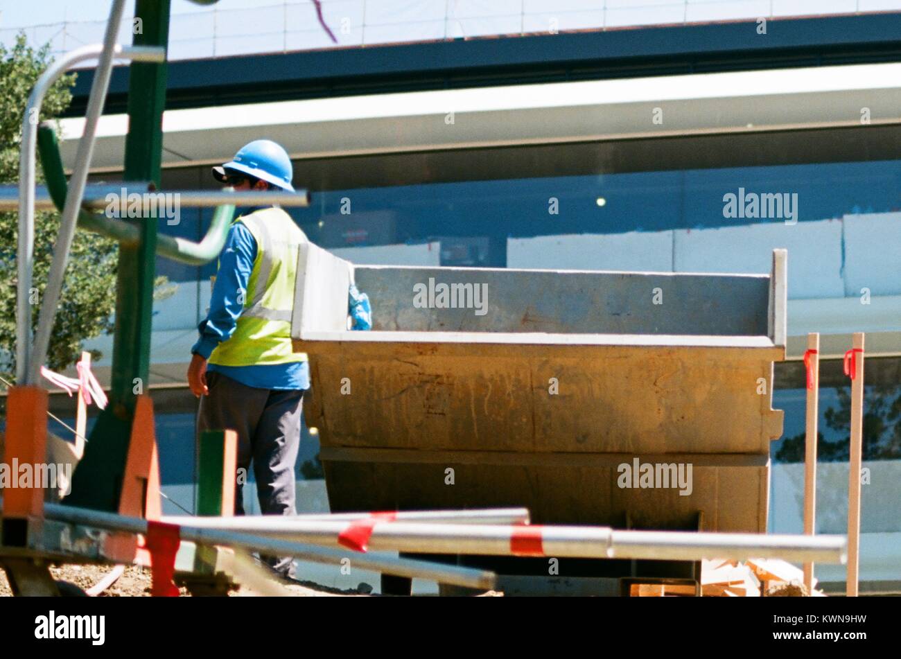 A construction worker stands with a dumpster, with windows of the main building visible blocked with white paper and painter's tape, at the Apple Park, known colloquially as 'The Spaceship', the new headquarters of Apple Inc in the Silicon Valley town of Cupertino, California, July 25, 2017. Stock Photo