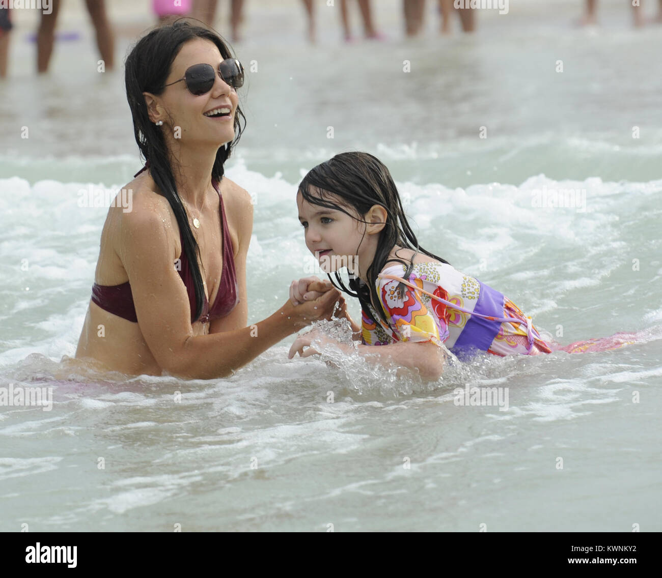 MIAMI BEACH, FL - JUNE 18: Katie Holmes and Suri Cruise had a fun day out on beach today in Miami, outside their hotel.  The famous mother and daughter pair played in the sand and splashed in the waves, entertaining themselves while Tom Cruise is busy filming the feature “Rock of Ages.”  Suri wasn’t quite prepared for the water, as she splashed around in a dress instead of a bathing suit. But, Katie Holmes rocked a red bikini, showing off a flat stomach and proving that she isn’t hiding a baby bump.   on June 18, 2011 in Miami Beach, Florida    People:  Katie Holmes Suri Cruise Stock Photo