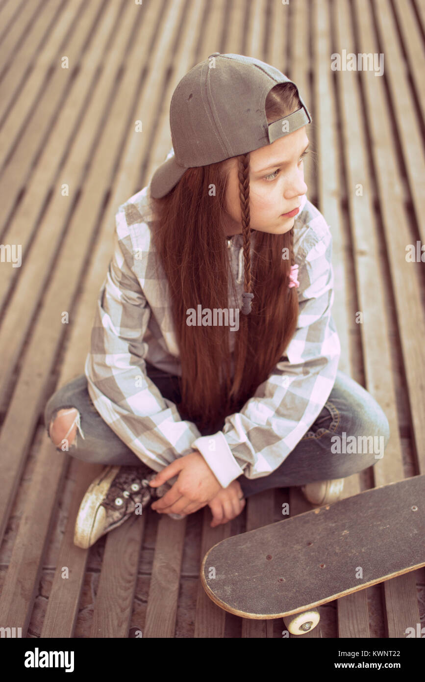 street style child girl with skateboard sitting on wooden planks floor Stock Photo