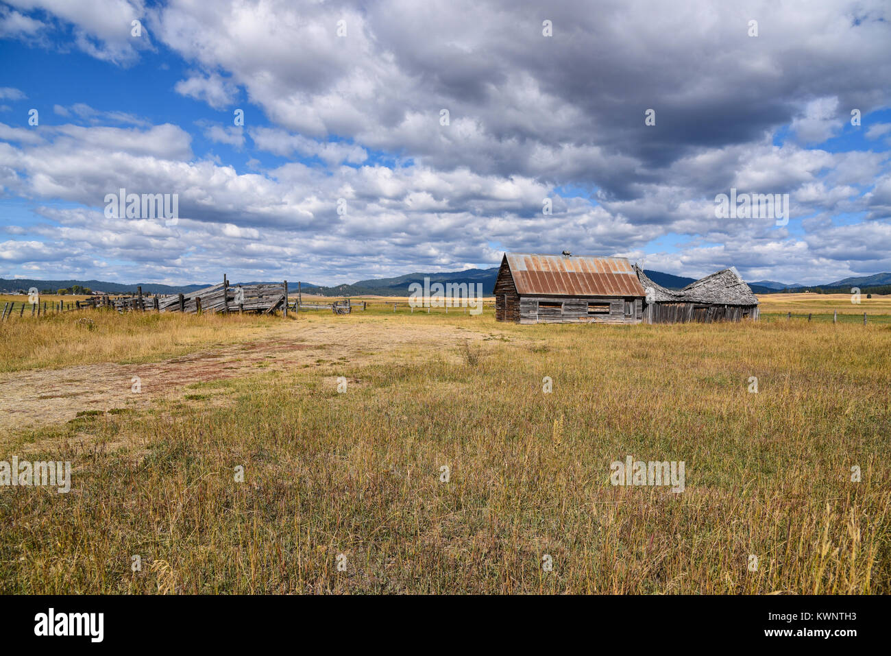 Abandoned wooden barn and farm buildings in a prairie field behind a fence next in Idaho state, USA on a sunny cloudy day Stock Photo