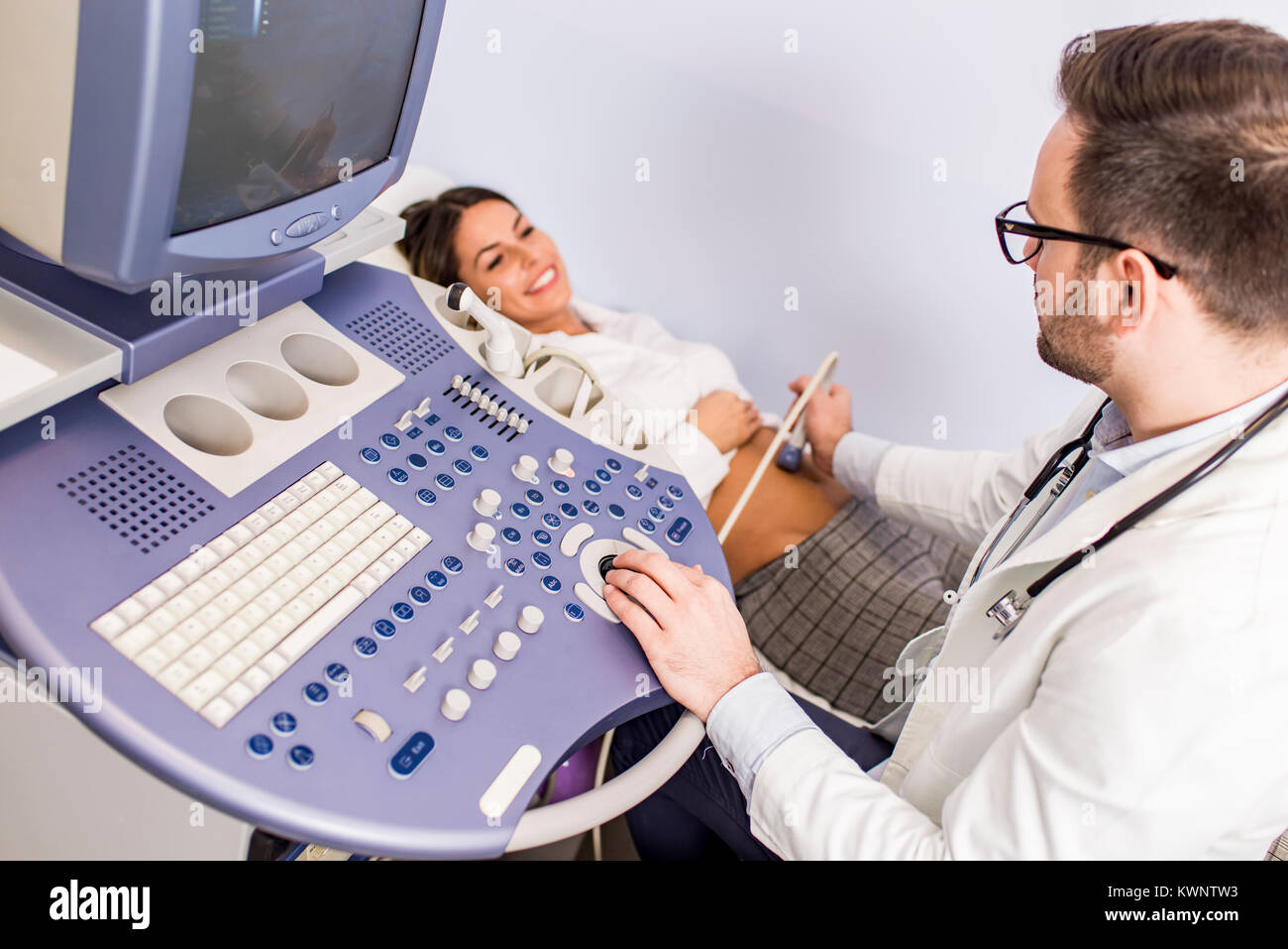Happy mid adult female patient going through abdomen ultrasound at clinic Stock Photo