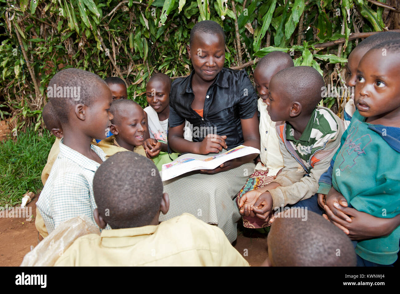 Young teacher reading a story to children gathered around her. Rwanda. Stock Photo
