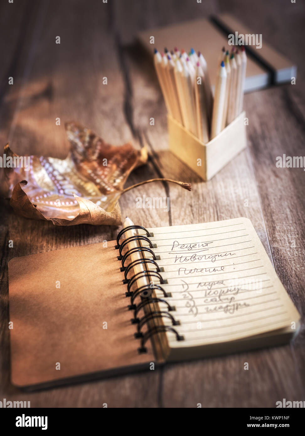 Open notebook with cookie recipe on a table with pencils and decorated marple leaf. This image is toned. Shallow DOF, focus on the writing. Stock Photo