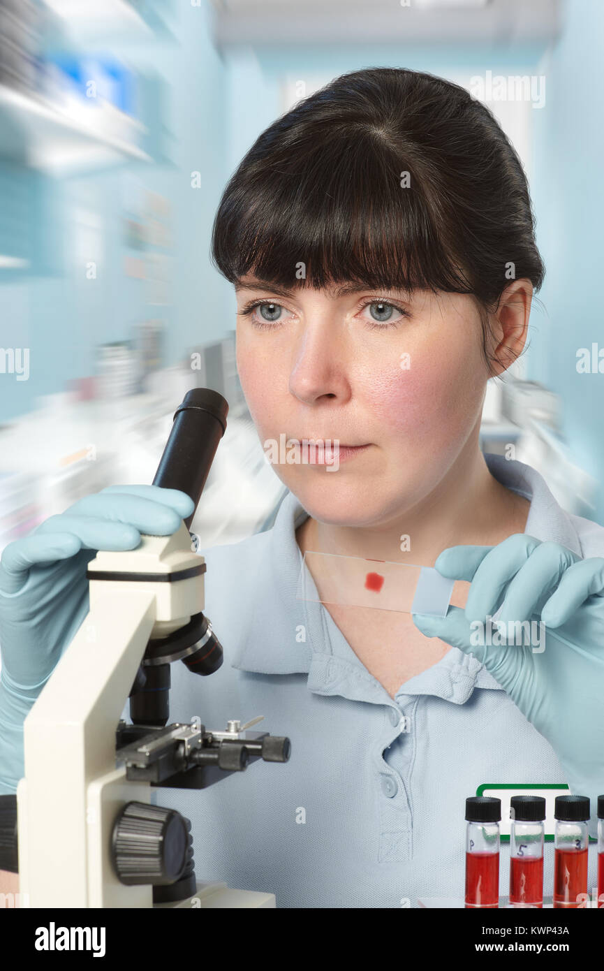 Portrait of a young female scientist analyzing red liquid samples under the microscope Stock Photo