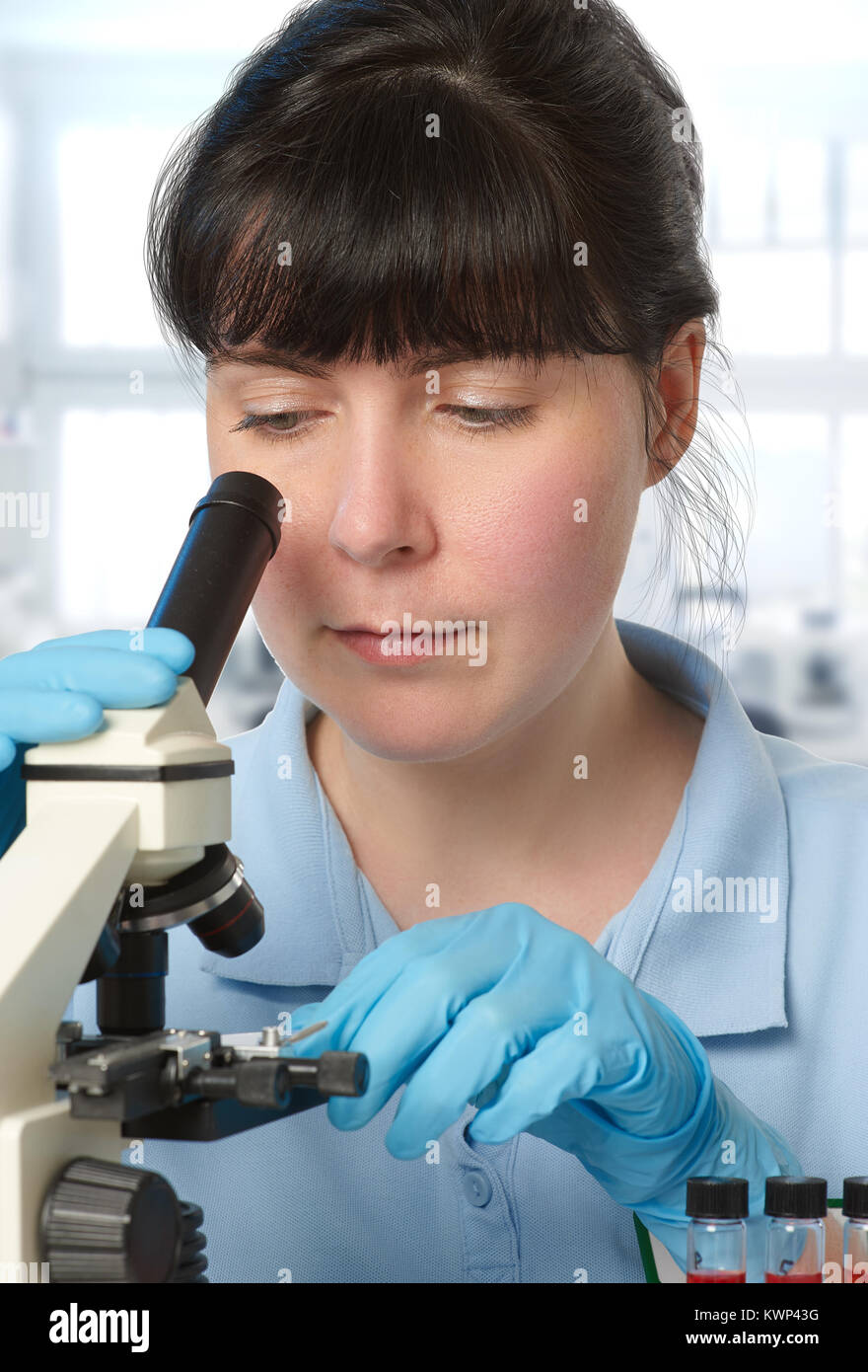 Portrait of a young female scientist analyzing red liquid samples under the microscope Stock Photo