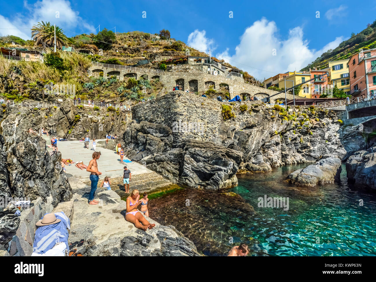 Tourists swim at the coastal harbor bay of the village of Manarola Italy, on a sunny day in Cinque Terre Italy Stock Photo