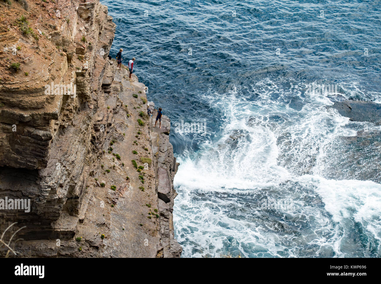 5 Boys climbing a Turimetta Headland cliff with waves crashing onto rocks below. Stock Photo