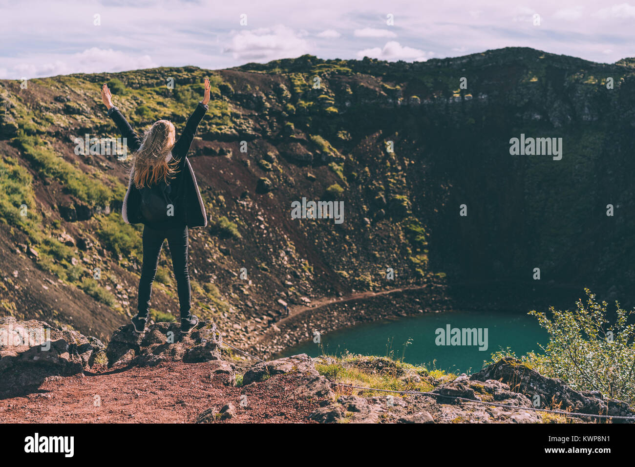 back view of girl standing with raised hands and looking at beautiful crater lake in Iceland Stock Photo