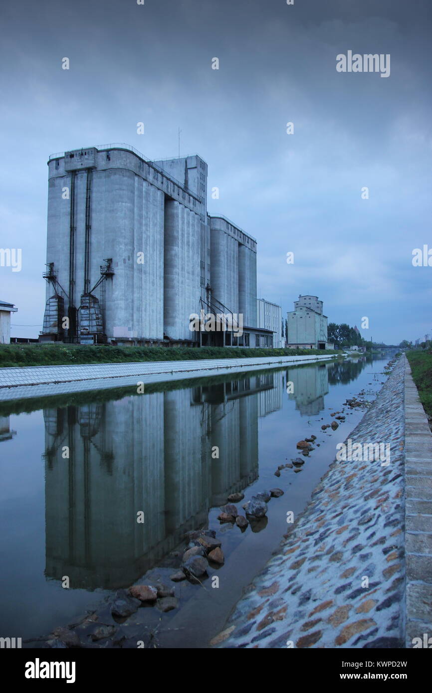 Stormy dark clouds over a cereal silo with water reflection in Bega river, near Timisoara, Romania Stock Photo