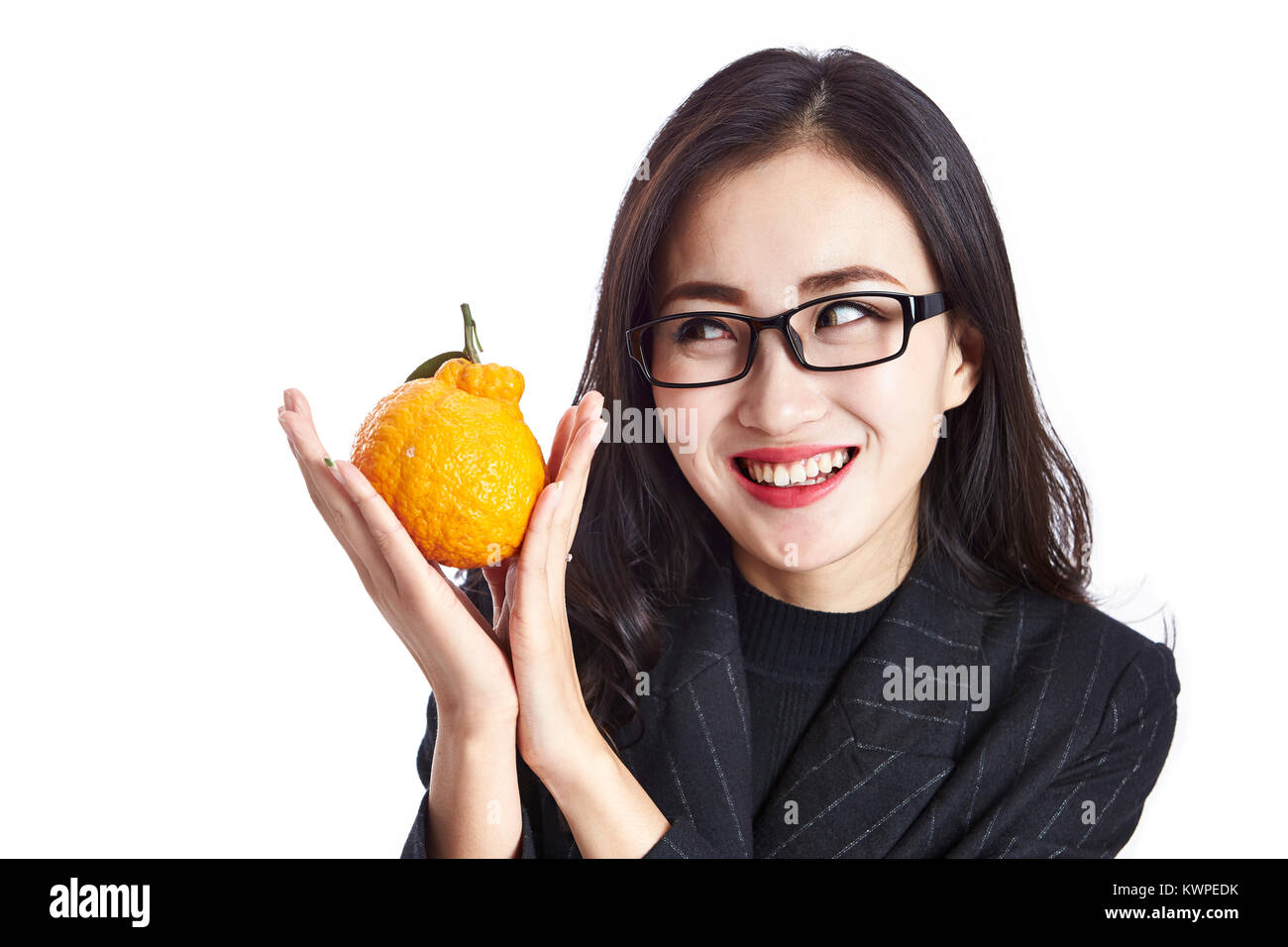 studio shot of a young asian business woman holding an ugli fruit, making a face, happy and smiling, isolated on white background. Stock Photo