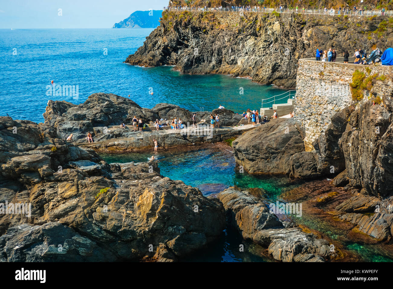 Tourists and locals enjoy swimming in the shallow sea water off Manarola Italy on a sunny day on the coast of Cinque Terre Italy Stock Photo