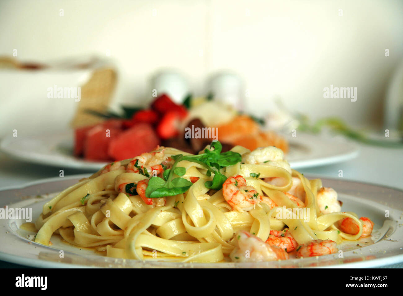 Close-up of shrimp pasta dish with a fruit salad dessert Stock Photo