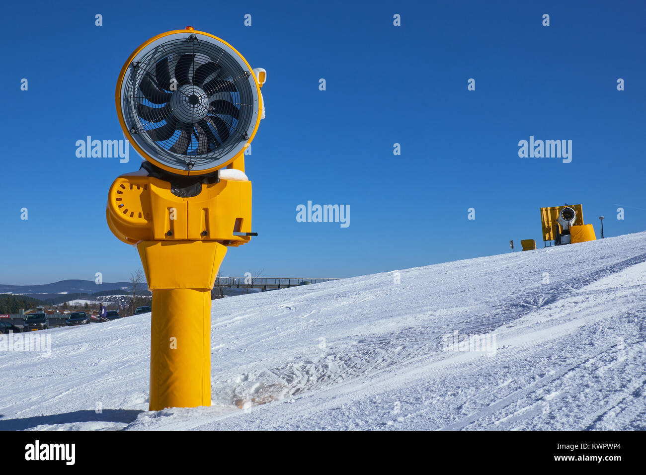 Two turned off yellow snow cannons on a piste at Ski Carousel Winterberg against a clear blue sky Stock Photo