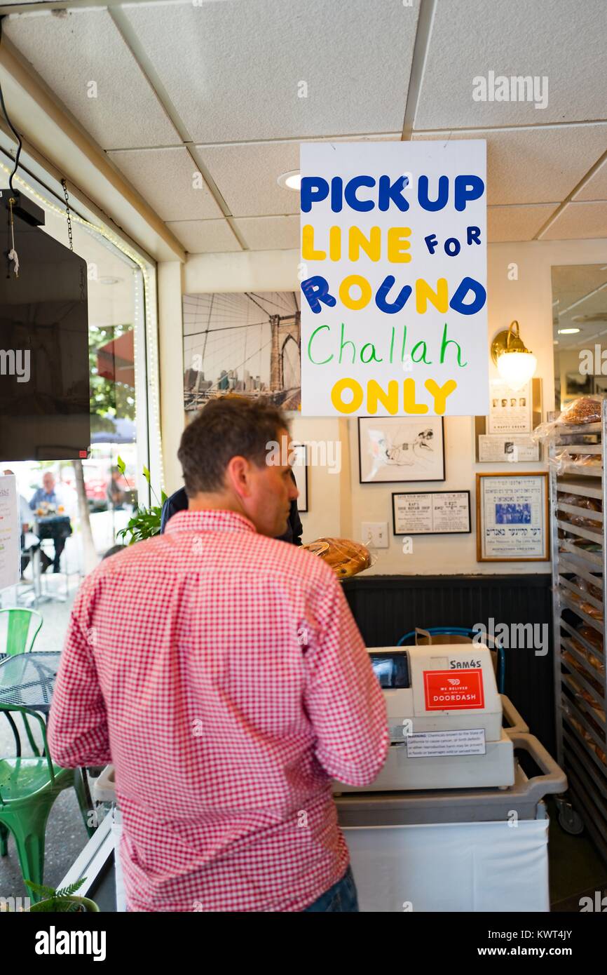 A man waits in line to pick up a challah bread for the Jewish high holiday of Rosh Hashanah (New Year) at a special counter with a sign reading 'Pickup line for round challah only' at Izzy's Brooklyn Bagels, a Jewish kosher deli and bakery in the Silicon Valley town of Palo Alto, California, September 20, 2017. In the Jewish religion, the round challah represents the cycle of the year. Stock Photo