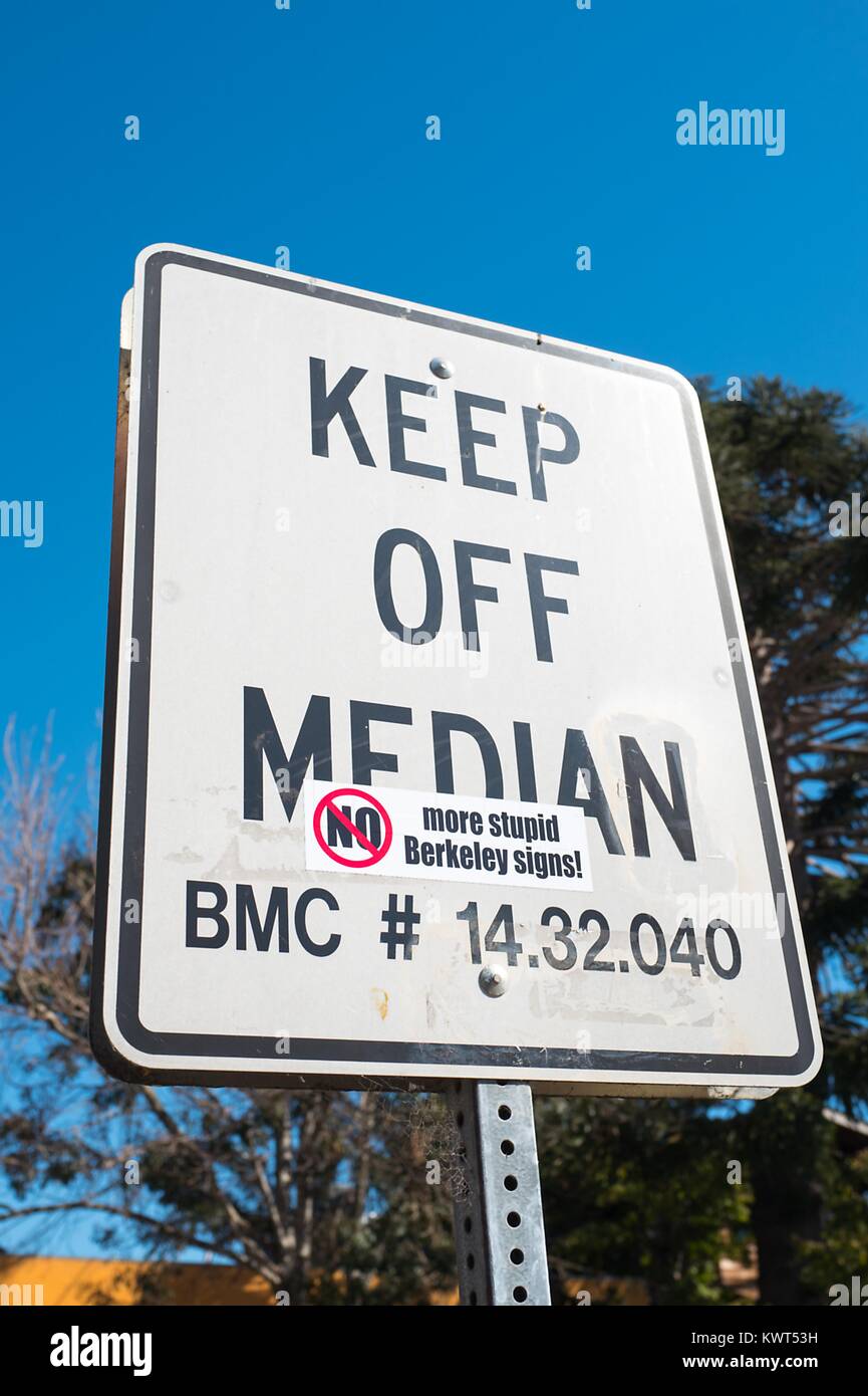 Road sign reading 'Keep Off Median', on which someone has placed a sarcastic decal reading 'No More Stupid Berkeley Signs', on a road median which is a popular picnic area for UC Berkeley students, in the Gourmet Ghetto (North Shattuck) neighborhood of Berkeley, California, October 6, 2017. () Stock Photo