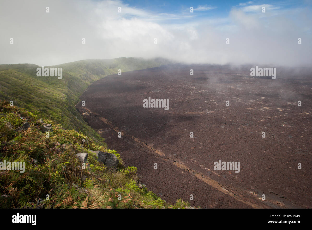 Clouds roll in at the top of Sierra Negra volcano. The lava-covered caldera is visible below. Stock Photo