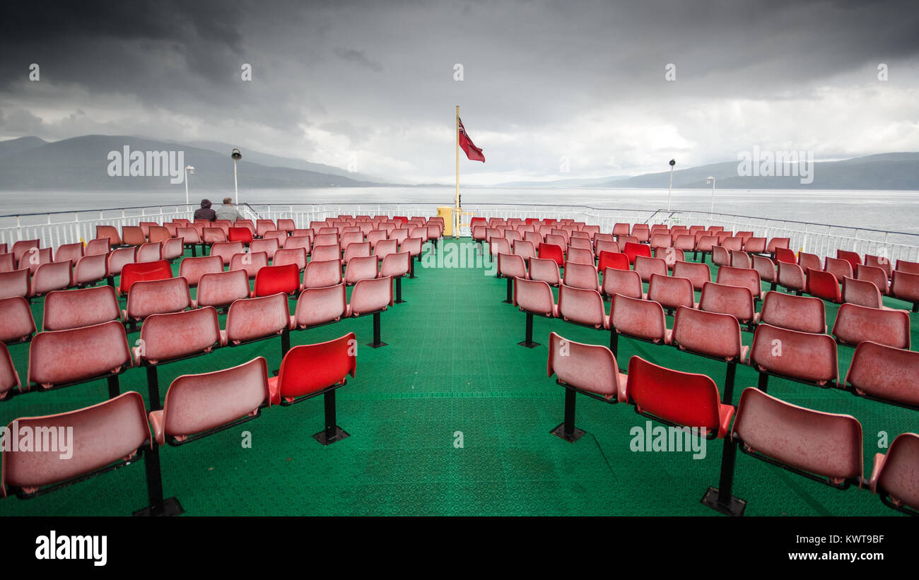 A couple sit alone in the rain on the open deck of the CalMac ferry from the Isle of Mull to Oban in Scotland's West Highlands and Hebridean Islands. Stock Photo
