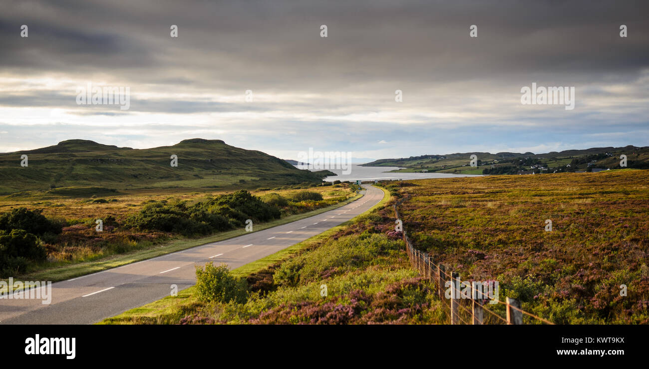 The A87 road runs through pastures and heather moorland towards Loch Snizort and the Trotternish Peninsula on Scotland's Isle of Skye. Stock Photo