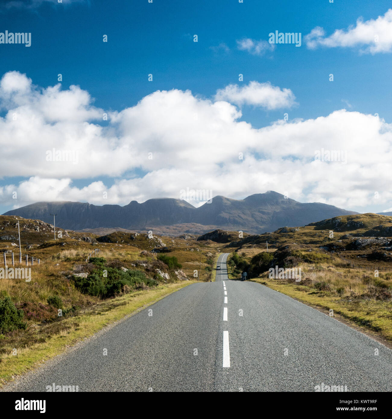 Quinag mountain rises in the distance behind the A837 road, part of the North Coast 500 touring route in Assynt in the remote Sutherland county in the Stock Photo