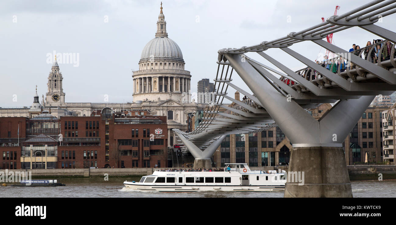A river cruise ship sails under the Millennium Bridge on the River Thames in London, England. The dome of St Paul's Cathedral stands in the background Stock Photo