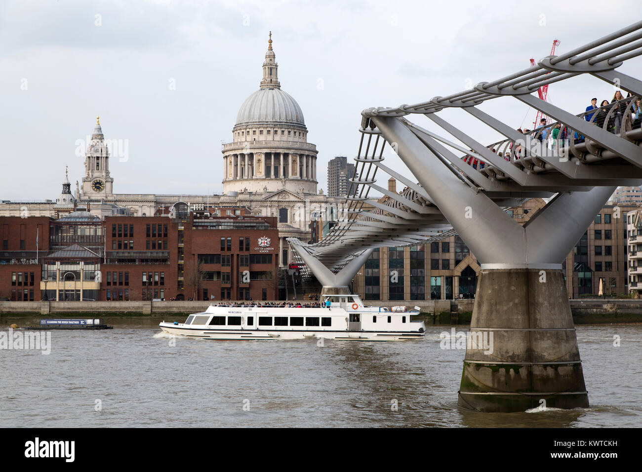 A river cruise ship sails under the Millennium Bridge on the River Thames in London, England. The dome of St Paul's Cathedral stands in the background Stock Photo