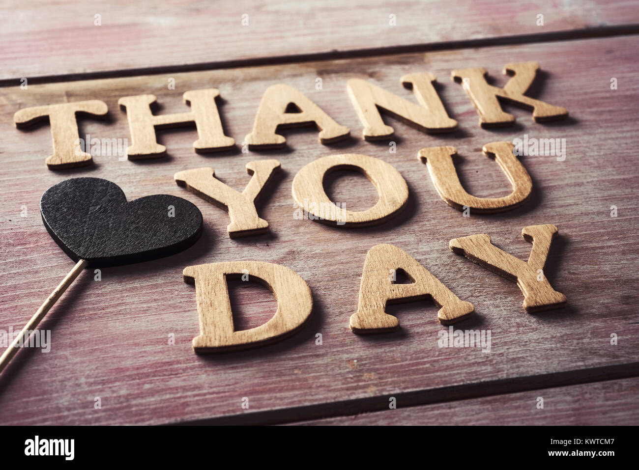 some wooden letters forming the text thank you day and a heart attached to a stick on a rustic wooden surface Stock Photo