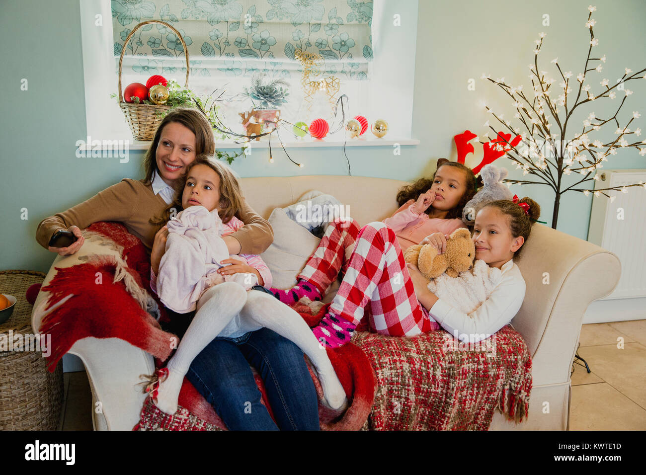Three little girls are relaxing on the sofa with their mother at christmas time, watching the television. Stock Photo