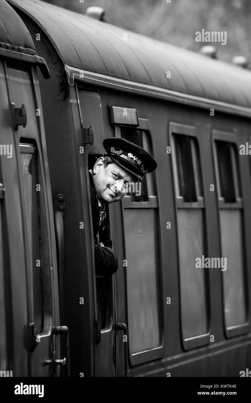 Black and white close-up shot of smiling guard, with SVR cap, leaning out of window to check all is safe for train to proceed on its journey. Stock Photo